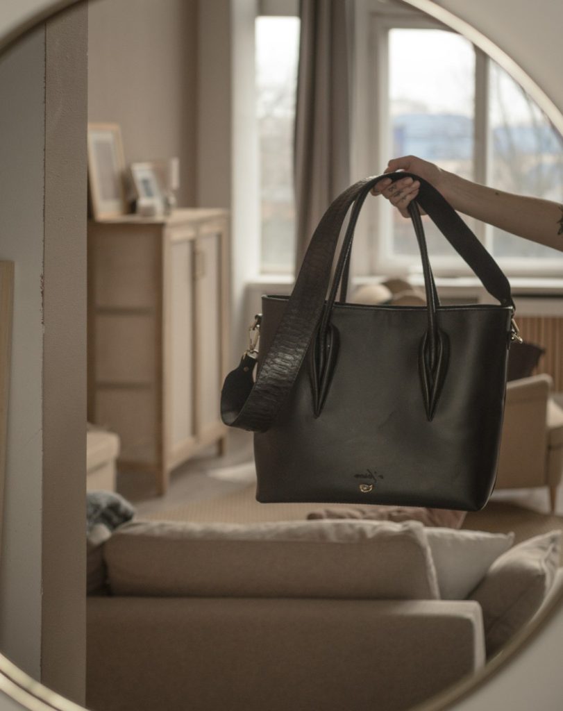 a-woman-holding-a-black-purse-in-front-of-a-mirror-kbs4ktx1m3k
