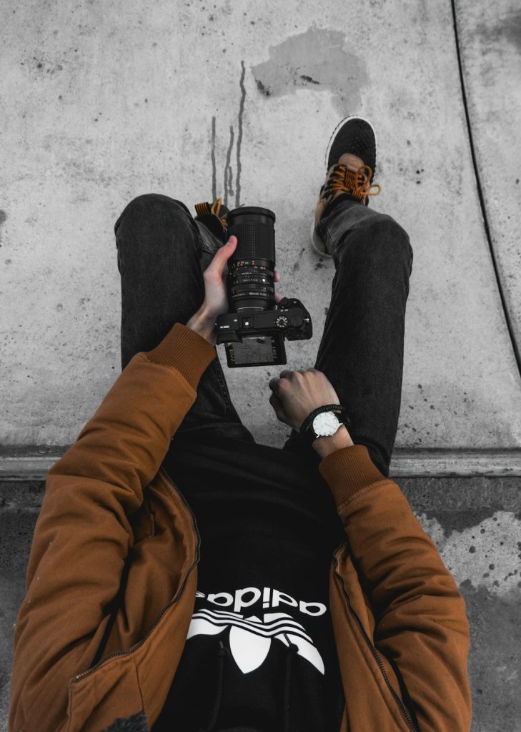 man-sitting-on-concrete-ground-while-holding-dslr-cameraa-le6ntwv9h9y